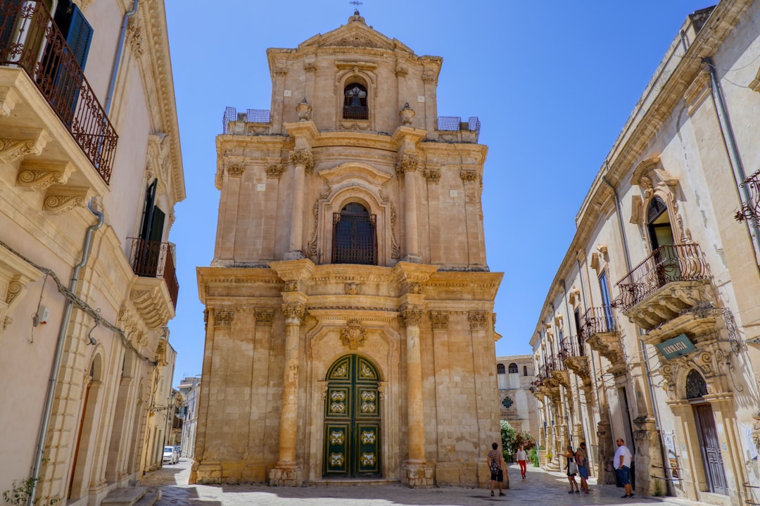 Street scene in a Sicilian hill town beside an Arab-Norman church facade with geometric limestone banding